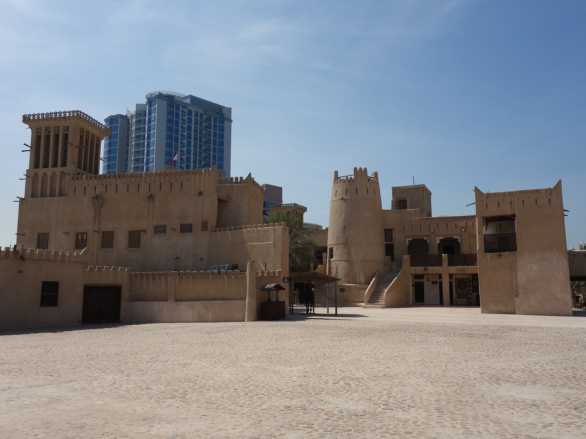 Ajman Fort courtyard with wind tower and modern high-rise buildings behind it, Ajman, United Arab Emirates